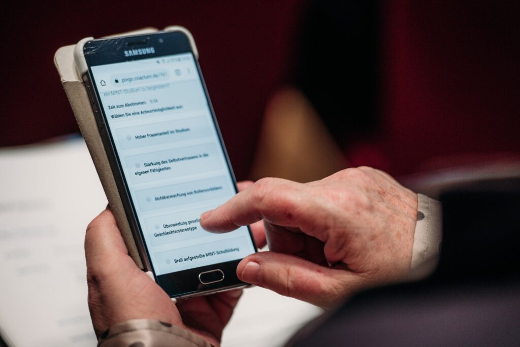 Ein älterer Mann nimmt während der Transfertagung "Erfolg mit MINT" des Bundesminsteriums für Bildung und Forschung 2020 auf seinem Smartphone an einer Live-Umfrage teil