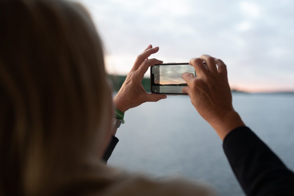 Eine Person macht mit ihrem iPhone ein Foto vom Sonnenuntergang zur Spargelfahrt des Seeheimer Kreises 2023 auf dem Berliner Wannsee