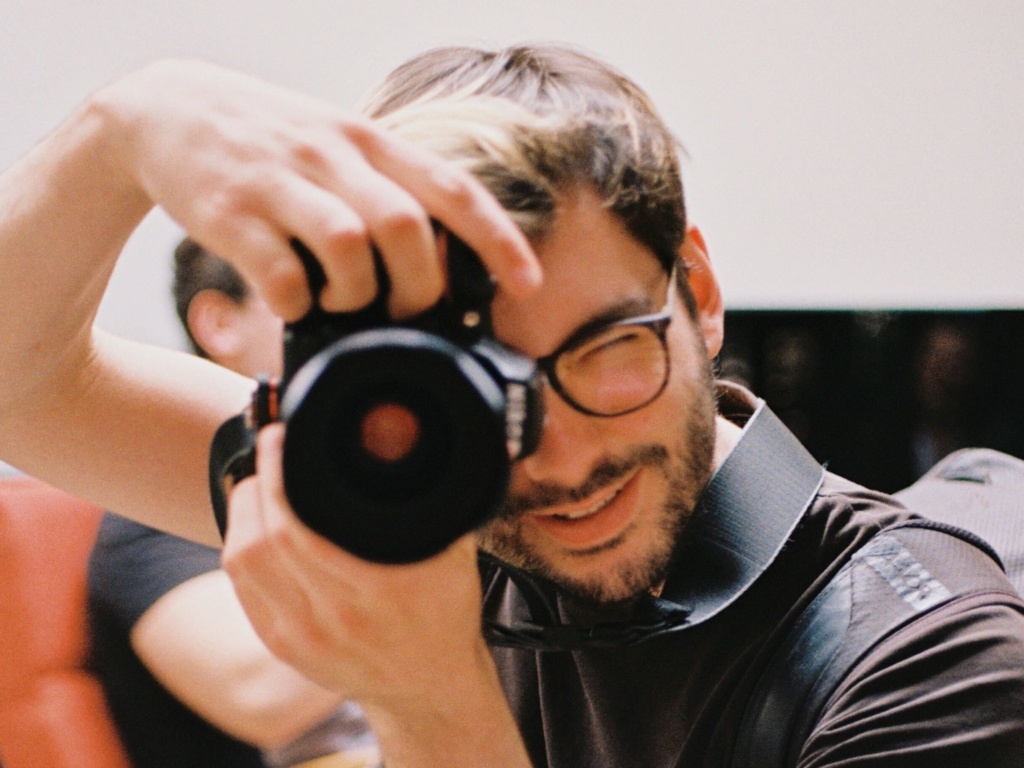 Portrait Kurt Sauer beim Fotografieren Ein Mann mit Brille, Kurt Sauer, macht ein Foto mit einer Kamera.